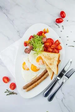 Scrambled eggs with vegetables, cherry tomatoes, bread, herbs and sausages on a Foto stock