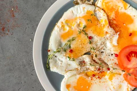Scrambled,  fried eggs with thyme and tomato and spices on a plate, on a gray Stock Photos
