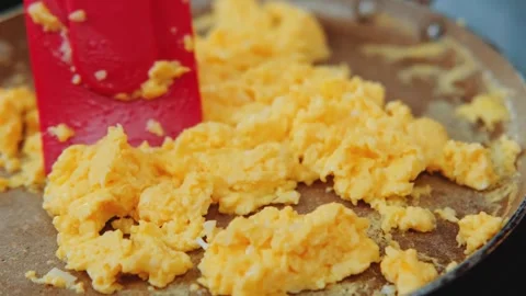 Scrambling eggs with red spatula in frying pan indoors Stock Footage 342831055