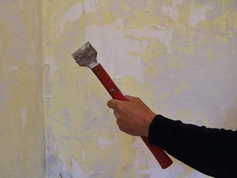 Scraper in hand against the background of old torn wallpaper Stock Photos
