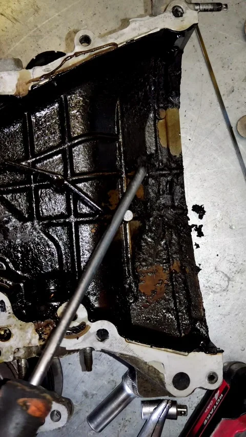 Scraping thick black oil sludge from a metal engine part 스톡 동영상 334321643