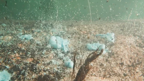 Scraps fall down and melt in lake water with pebbled bottom Stock Footage 243299887