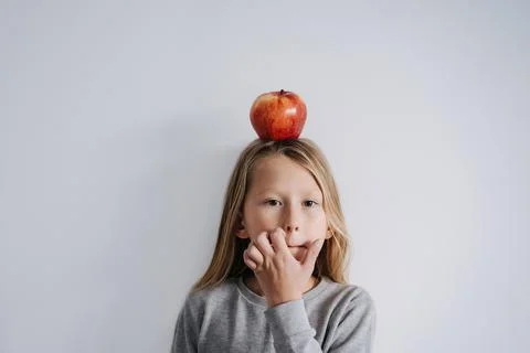 Scratching his face boy with an apple on his head. Over white wall. Stock Photos