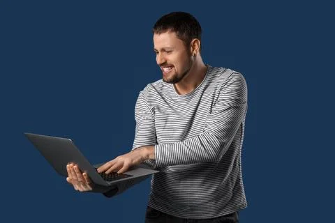 Screaming young man using laptop on dark blue background Stock Photos