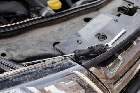 The screwdriver and the key are on the open dusty hood of the car Stock Photos