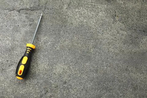 Screwdriver with black handle on grey textured table, top view. Space for tex Photos