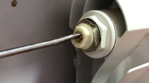 Screwdriver Opens Radiator Valve Releasing Water Stream in Home Heating System Stock Footage 329455865