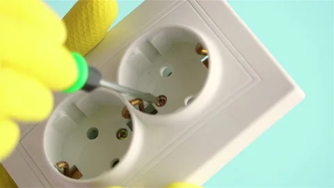 Screwdriver tool screwing  electric socket outlet repair yellow glove hand Stock Footage 149724924