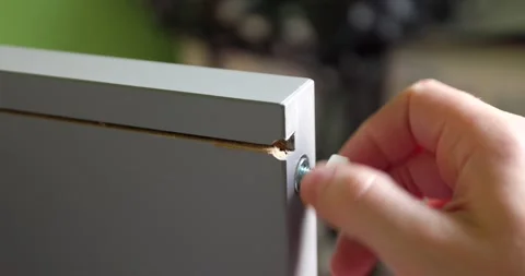 Screwing a screw with white head to a piece of wooden grey furniture while as Stock Footage 150202138