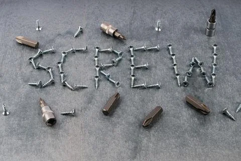 Screws and screwdriver bits arranged to spell 'SCREW' on gray surface Stock Photos