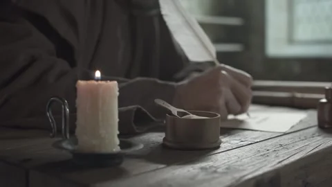 Scribe dipping a long feather quill into a clay inkwell and writing on a page Stock Footage 339232359