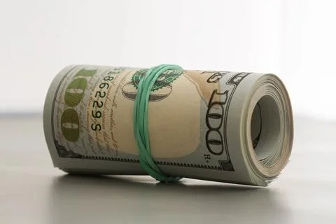 Scroll of dollar bills pulled by green rubber lies on light surface Foto stock