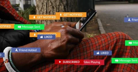 Scrolling man viewing notifications on phone, sitting by tree on path, Stock Photos
