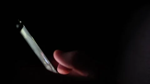 Scrolling through the phone in the dark with only the screen light softly illumi Stock Footage 313842868