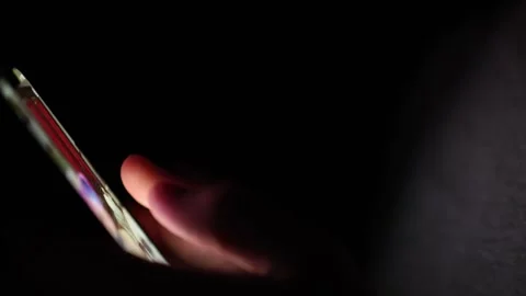 Scrolling through social media feed late at night in the dark lit only by the so Stock Footage 313842865
