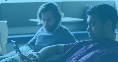 Scrolling two men holding smartphone and using tablet on lounge couch, plaid Stock Photos