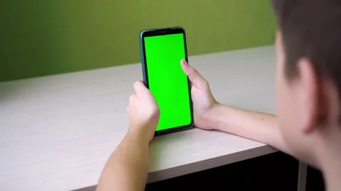 Scrolls with his finger on the touch screen. a teenager is sitting with a green Stock Footage 166524225