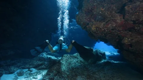 A scuba diver exploring coral caverns with ambient light rays - Grand Cayman Stock Footage 107831713