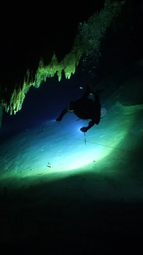 Scuba diver with a flashlight exploring a dark underwater cave with stalactites Vídeos de archivo 331341138