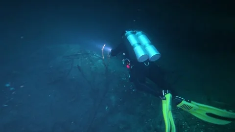 Scuba diver with a flashlight exploring a dark underwater cave in a cenote 스톡 동영상 339219905
