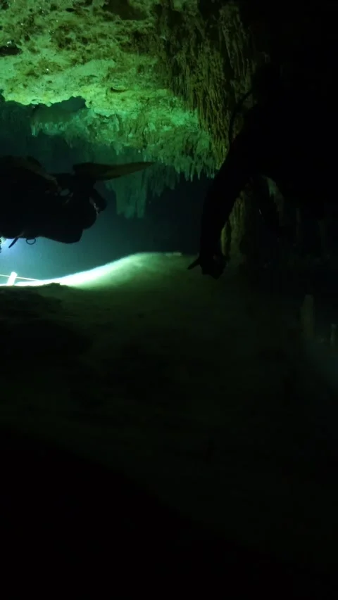 Scuba diver with a flashlight exploring a mysterious underwater cenote with Stock-Footage 332002531
