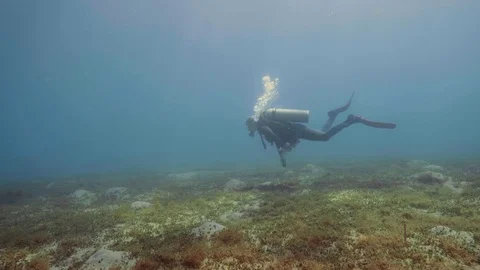 Scuba diver floating on sea bottom and waving hand to camera, underwater view Stock Footage