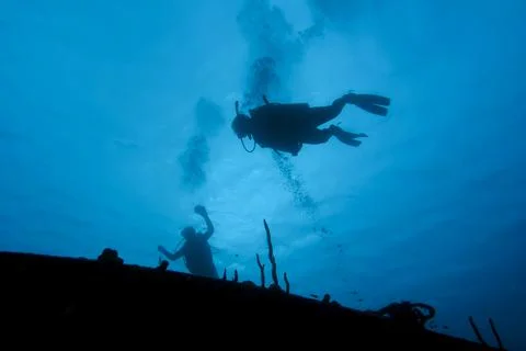 SCUBA diver hover over a shipwreck in silhouette Stock Photos