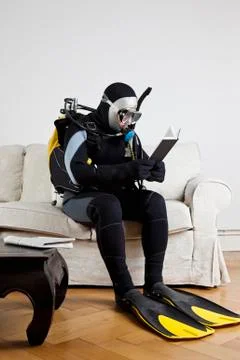 A scuba diver sitting on a couch reading a book Stock Photos