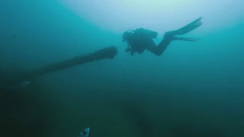 Scuba diver swims in front of sunken ship gun, under water shot Stock Footage 167055873