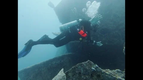 Scuba diver in a wetsuit exploring the remains of a sunken shipwreck deep in the 스톡 동영상 336243532
