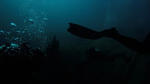 SCUBA divers explore a ship wreck in blue water as seen from a GoPro Stock Footage 115011391