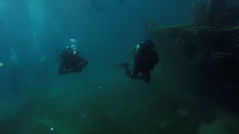 SCUBA divers explore a ship wreck in blue water as seen from a GoPro Stock Footage 115011762