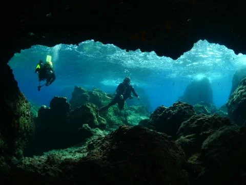 Scuba divers exploring cave underwater Stock Photos