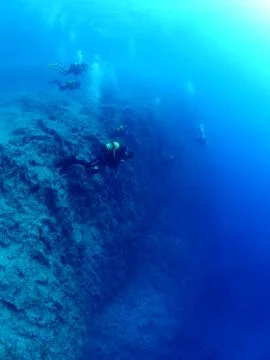 Scuba divers exploring rocks and reef underwater scenery Stock Photos