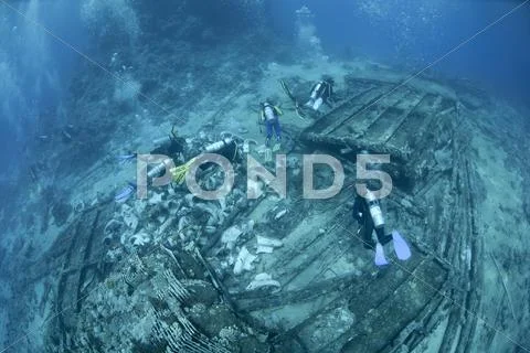 Scuba divers exploring the shipwreck debris on the ocean floor Stock Photos
