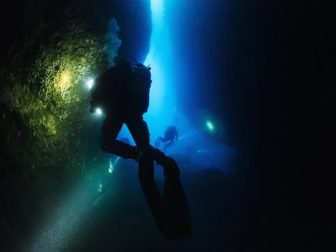Scuba divers with flashlights diving inside a cave Foto stock