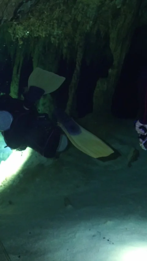 Scuba divers swimming through a dark underwater cave with flashlights, exploring Stock-Footage 332002238