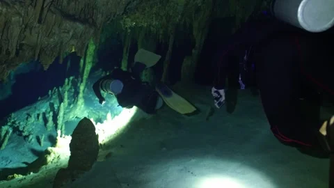 Scuba divers swimming through a dark underwater cave with flashlights, exploring Vídeos de archivo 332002344