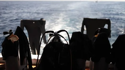 Scuba tanks wetsuits drying in sea breeze boat leaving trail calm water backlit  Stock Footage 310819861