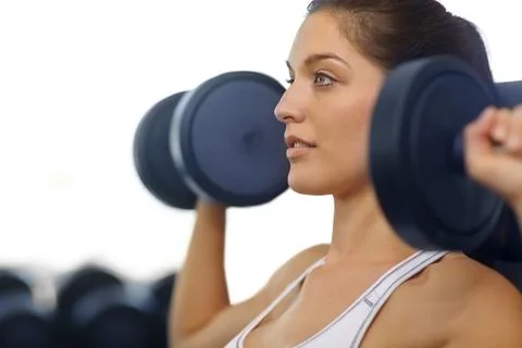 Sculpting her upper arms. A beautiful young woman exercising with weights at the Stock Photos