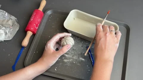 Sculptor refining the segmented shape of a tiny clay pumpkin by hand Stock Footage 345720845