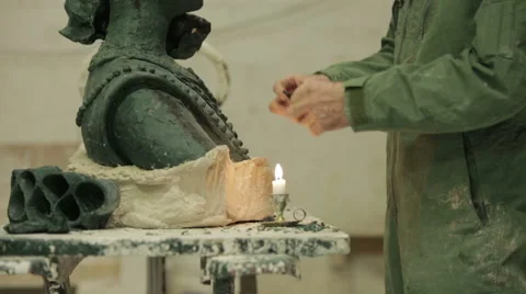 A sculptor using a candle to heat wax as he sculps a head to be cast in bronze Stock Footage 58638971
