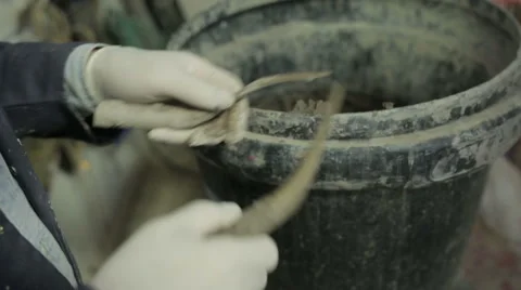 Sculptor in workshop using clay modelling tools with clay bucket in background Stock Footage 58641016