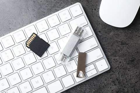 SD memory card, USB flash drives, keyboard and mouse on dark grey table, fl.. Stock Photos