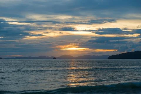 Sea and mountains in the rays of the setting sun, clouds in the sky Stock Photos