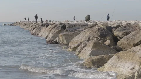 Sea that breaks on the rocks and in the background fishermen Stock Footage 123359658