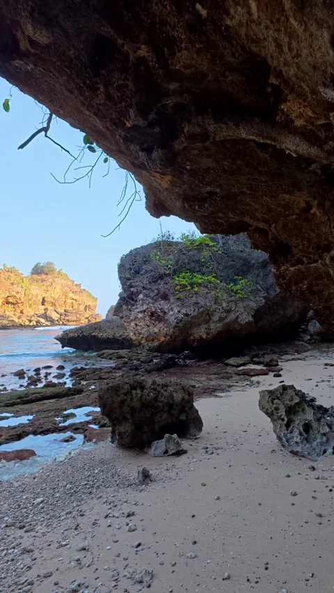 Sea cave opening frames secluded rocky beach and coastal blue water Stock Footage 346739495