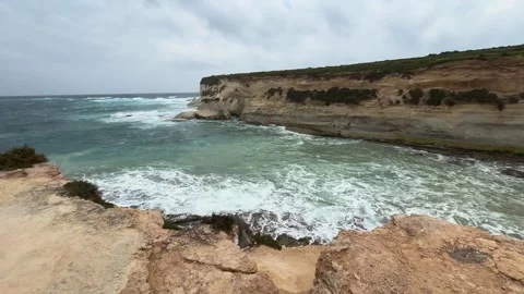 Sea cliffs enclose a small cove whitewater waves crash against rocky shoreline Видео 343678927
