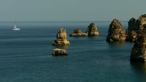 Sea cliffs small islands and sailboat in Algarve Stock Footage 119070027