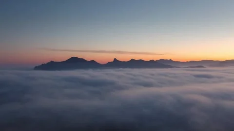 A sea of clouds at the base of the mountains as the sun sets Stock Footage 307704884